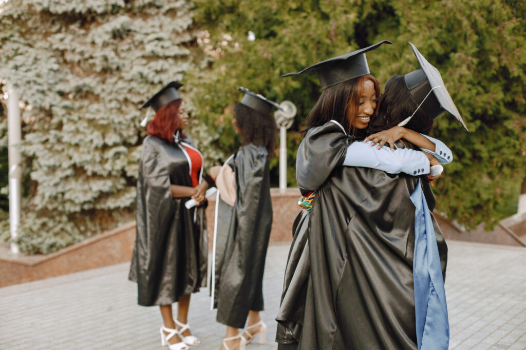 focus two young afro american female students dressed black graduation gown campus as background girls hugging scaled 1