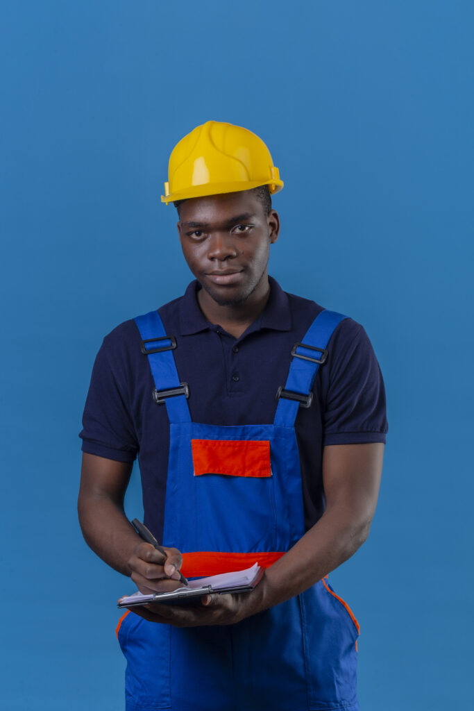 young african american builder man wearing construction uniform safety helmet holding clipboard pen going make notes with friendly smile standing blue